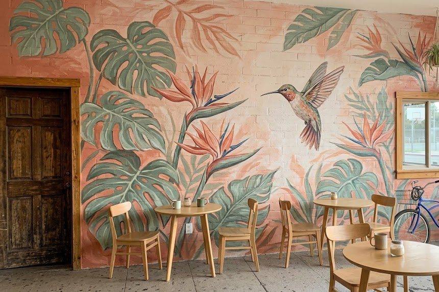 Soft botanical mural of monstera leaves, birds of paradise and a hummingbird on a coffee shop wall