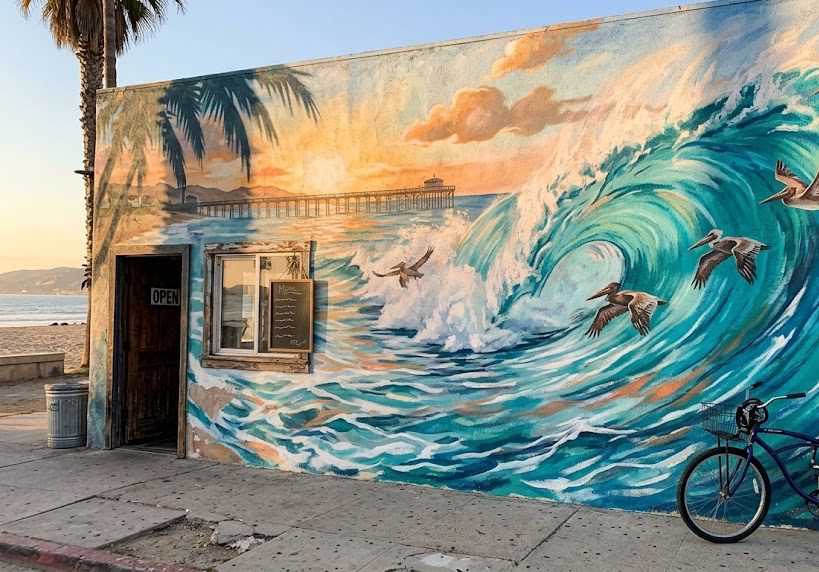 Mural of a curling turquoise wave with pelicans and a pier on the side wall of a beach bar